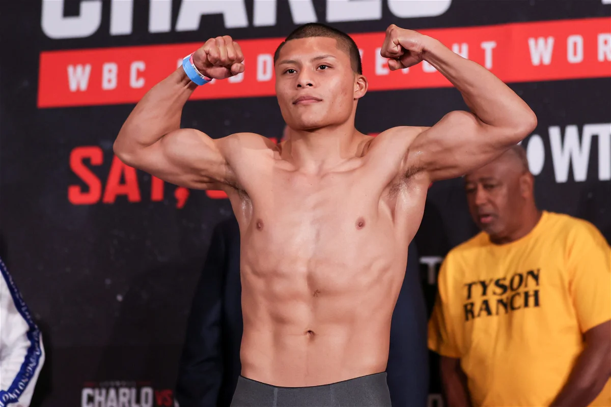 Isaac Cruz posa con los brazos flexionados en un escenario de boxeo