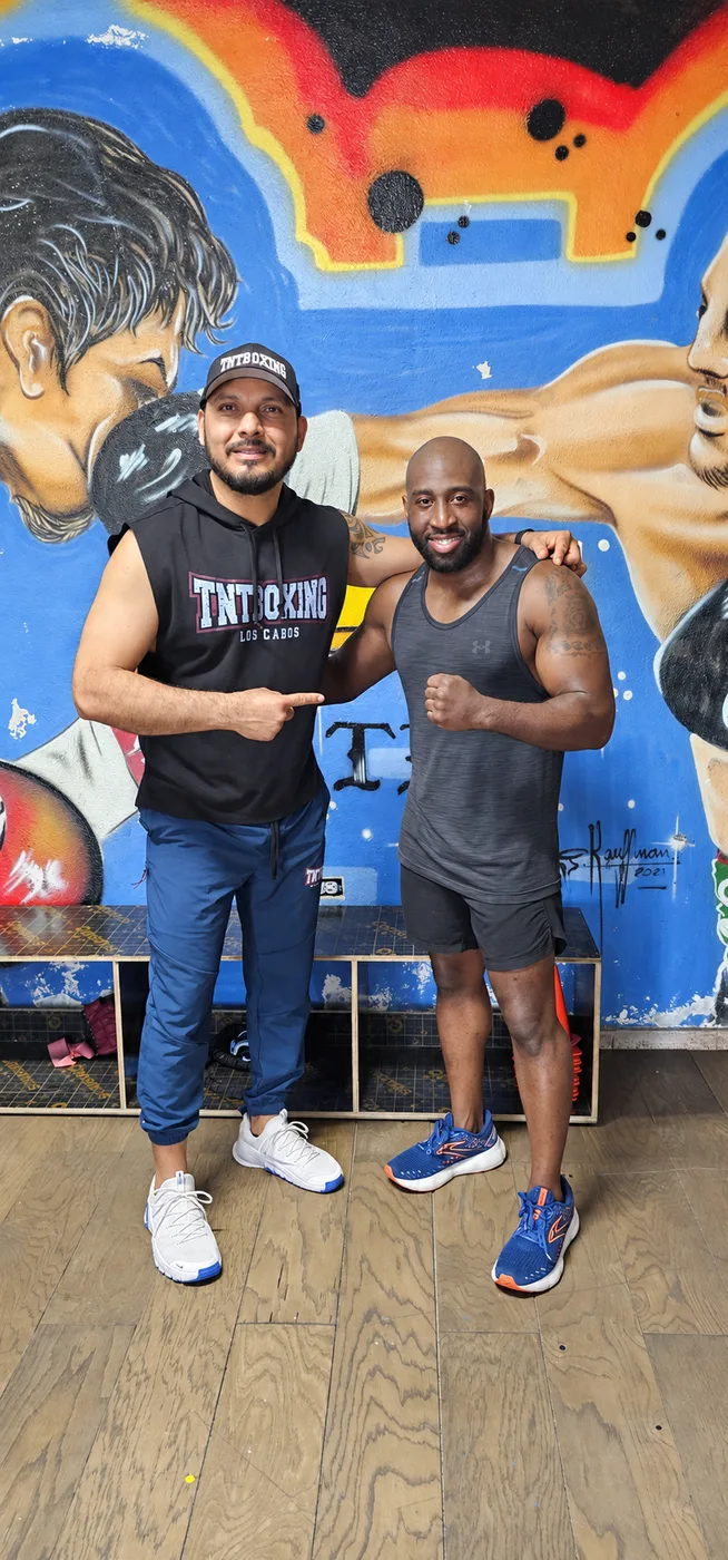 Dos integrantes de la comunidad de TNT frente al mural del gimnasio